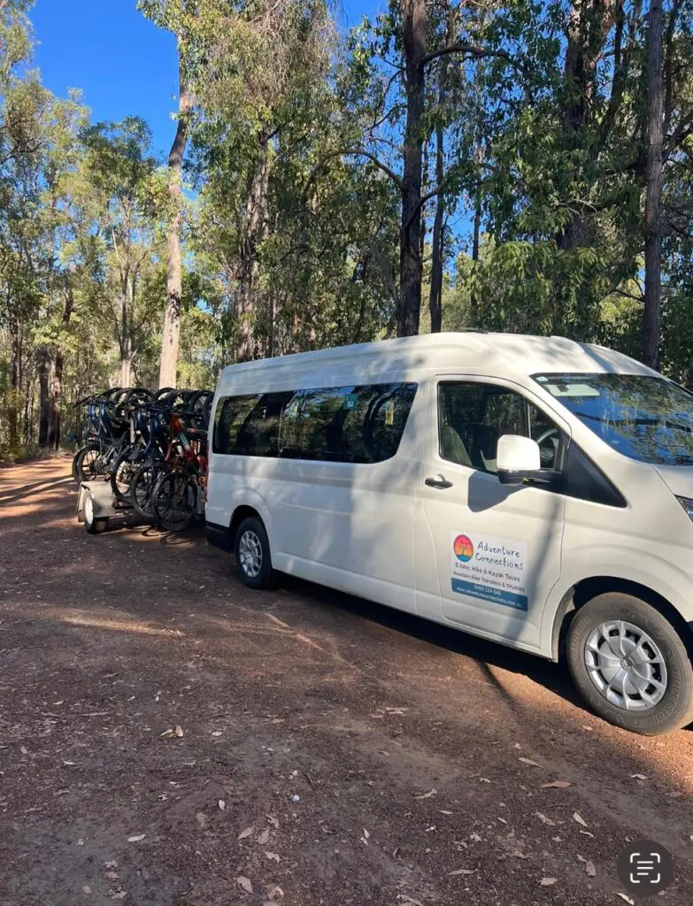 Transport Services 2 Adventure Connections van with a trailer carrying bikes, parked in a forest setting.